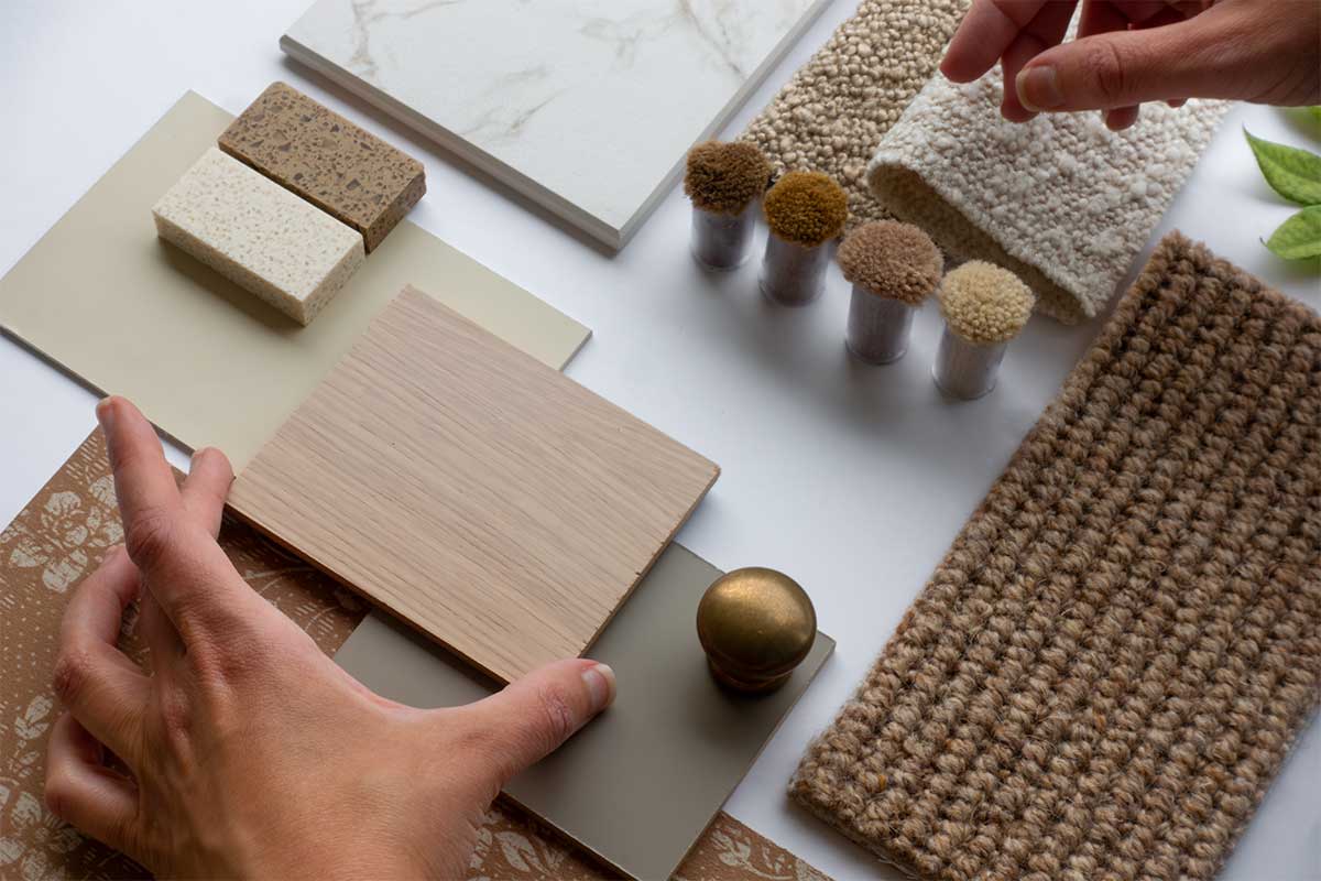 Hands of Interior Designer and Architect with Material Sample Board with Fabrics, Carrara Marble, Wood, and Wallpaper for Home Decoration Mood Board Concept
